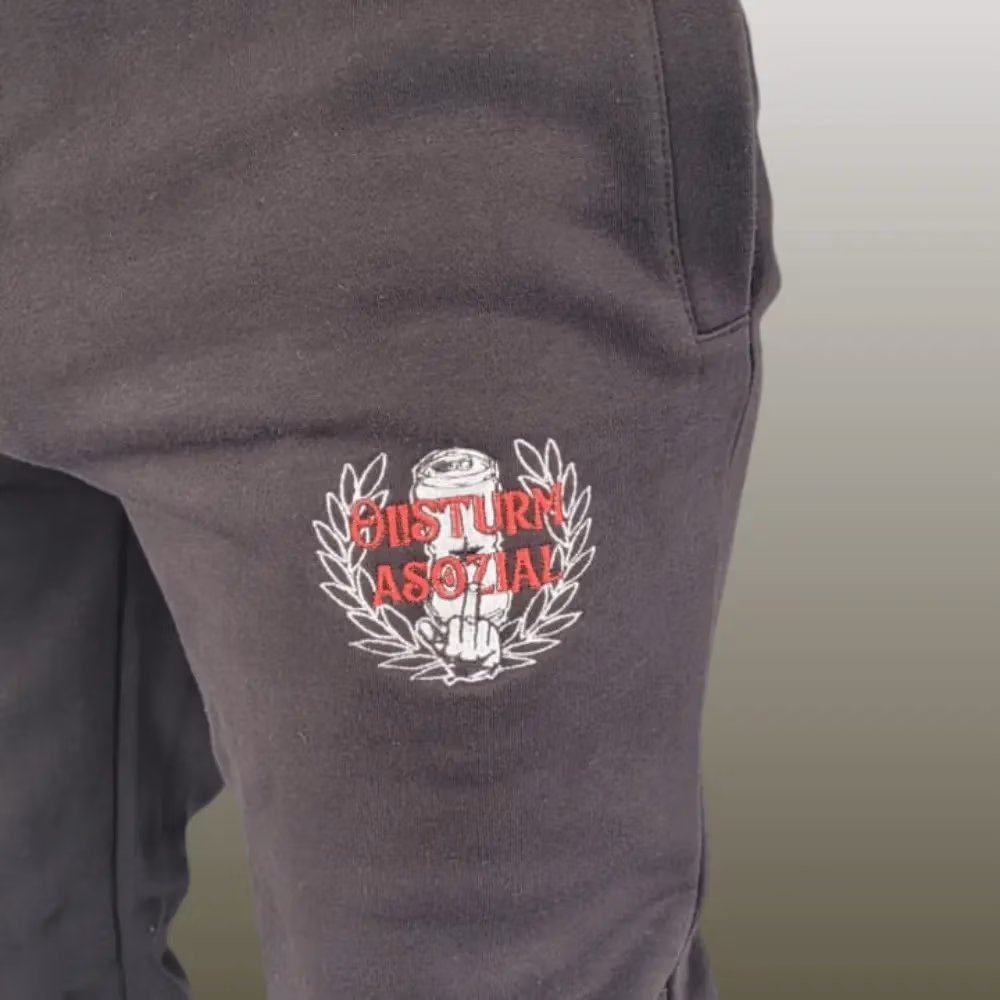 Schwarze Jogginghose mit Logo-Stick der Band Oi!Sturm Asozial auf dem linken Oberschenkel, Detailaufnahme.